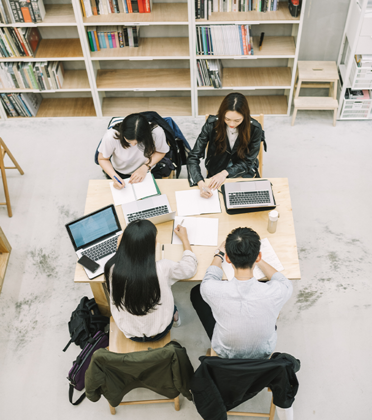 Students sat in library with laptops and pens and paper.