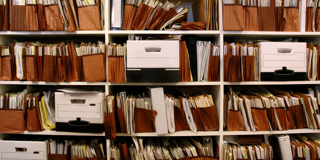 Archive documents stuffed into boxes on a shelf.