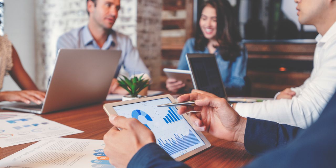 Colleagues sat around table discussing items on computers and paper.