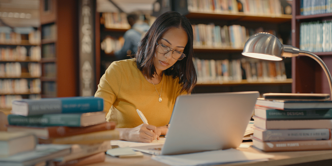 Student working at a desk with stacks of books.