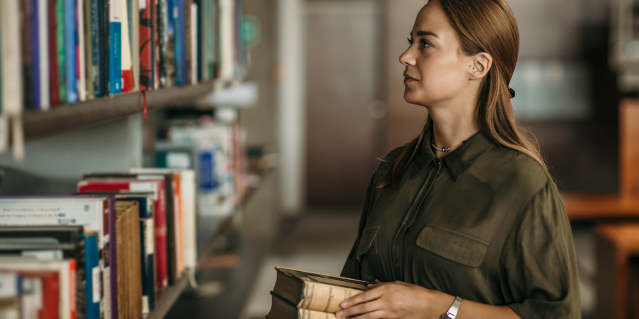 Person holding old books next to a shelve of books.