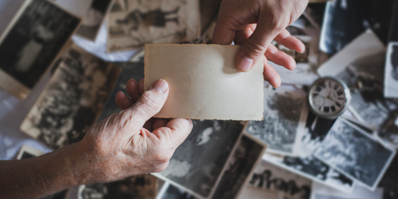 Old and young hand holding card across old photographs.