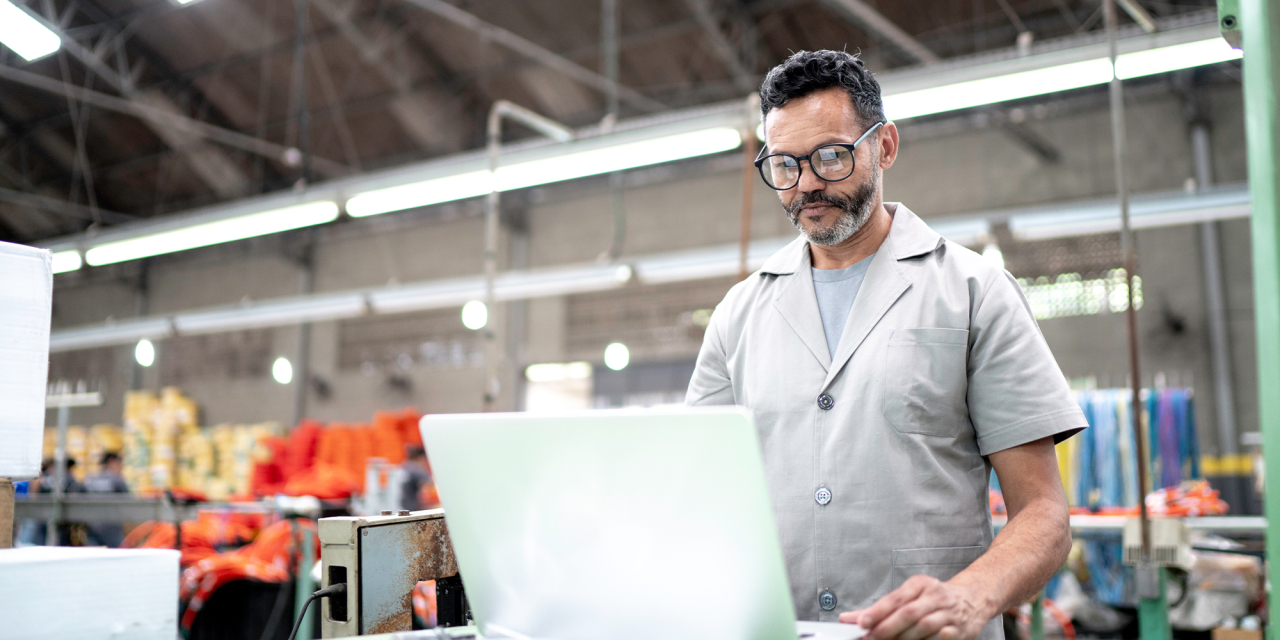 Man working on a laptop computer in a warehouse environment.